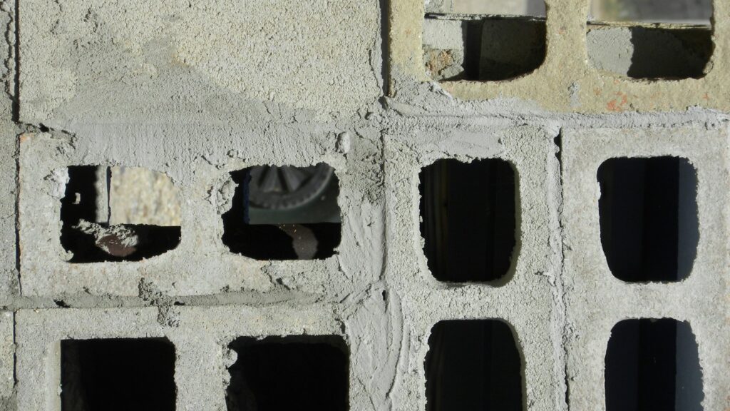 Gros plan de blocs de béton empilés en assises, leurs alvéoles creuses ouvertes sur le vide.